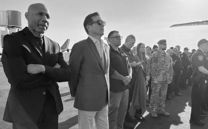 Black and white photo of a diverse group of individuals, including civilians and military personnel, standing on an airport tarmac.