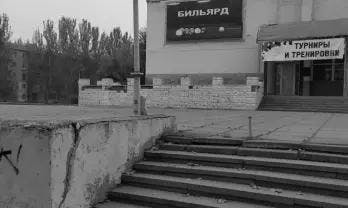 Black and white image showing a worn set of concrete stairs leading to a building with Cyrillic signage, indicating a place for tournaments and training